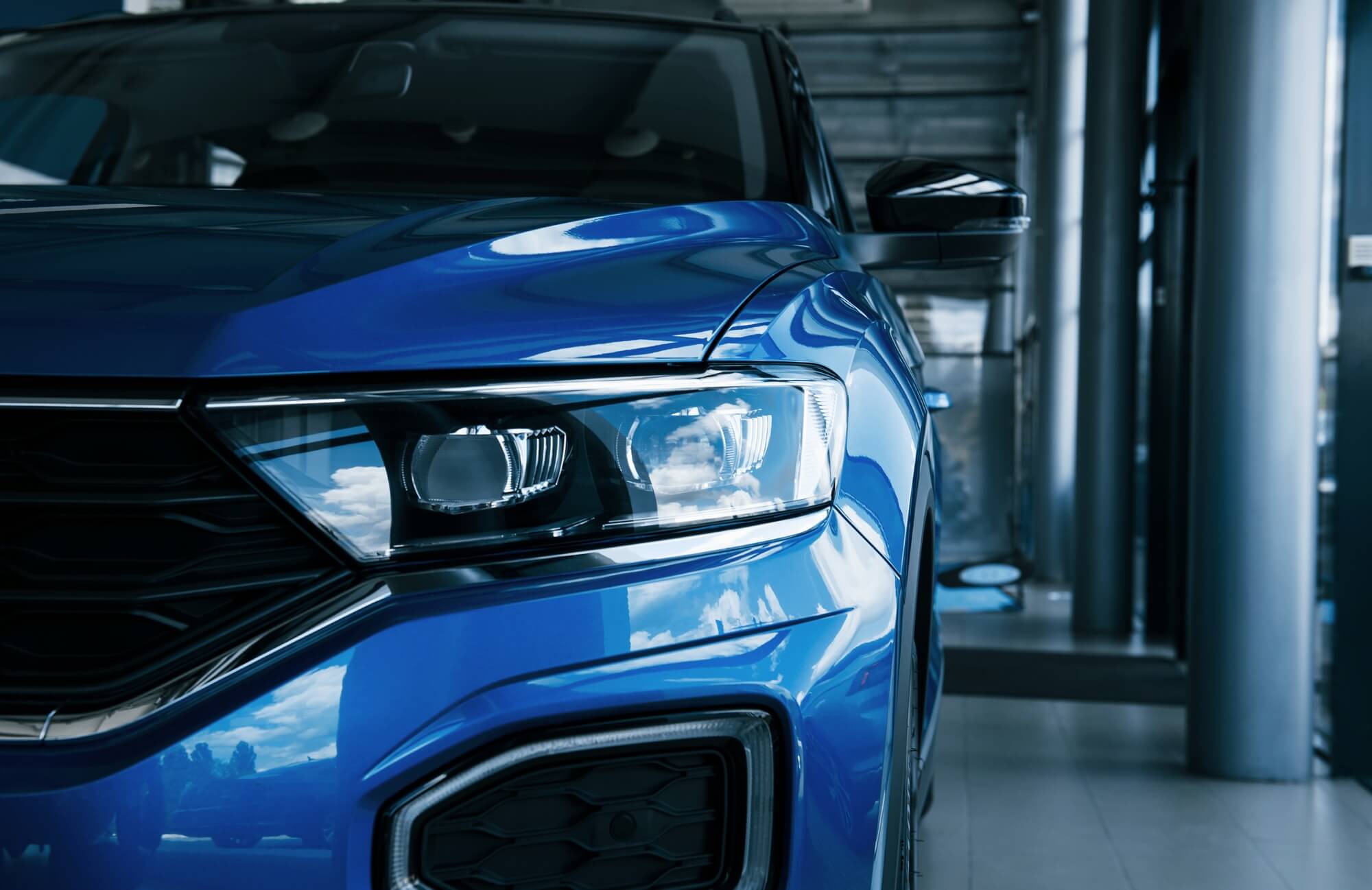 front part of brand new modern blue car parked at showroom reflection in the headlights